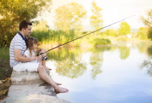 young father fishing on lake with his daughter